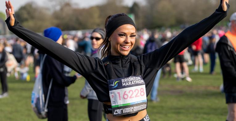 Woman in a headband and wearing a marathon number stands with arms out stretched