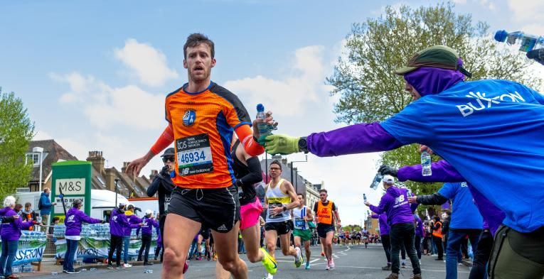 Person running in an orange top being handed a water by a volunteer