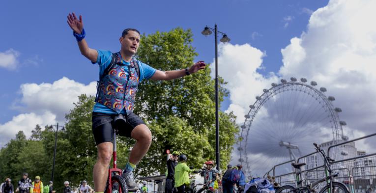 Man on unicycle by cycles past the London eye. 