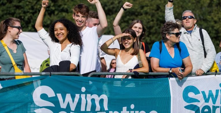 Group of people raise there hands in the air as they support the swimmers from behinde a barrier.