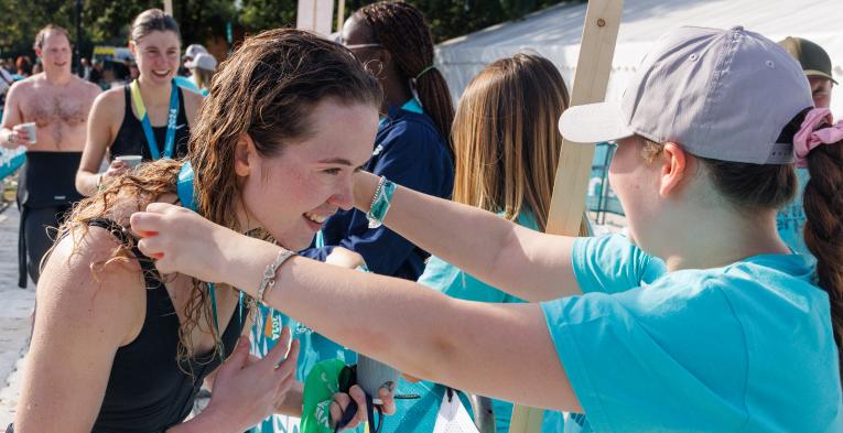 Volunteer puts the medal round the neck of a swimmer after they finish their swim.