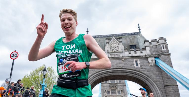 Runner in a green vest with a finger in the air celebrating. Tower bridge in the background. 