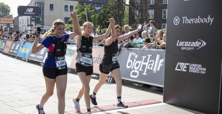 Three woman hold hands as they cross the finish line of the Big Half