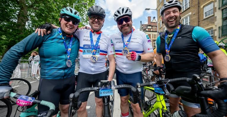 Four men with bikes, smiling and wearing ride london medals