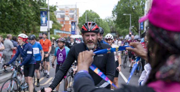 Volunteer holds out a medal to a cyclist finishing the RideLondon race.