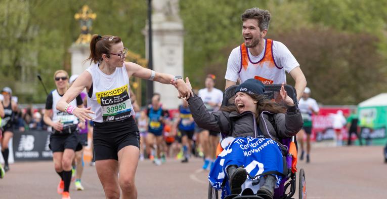 Man pushing women in a wheelchair with another women holding the hand of the women in the wheelchair. 