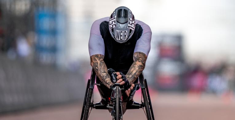 David Weir crossing the finish line lent over the front of his wheelchair