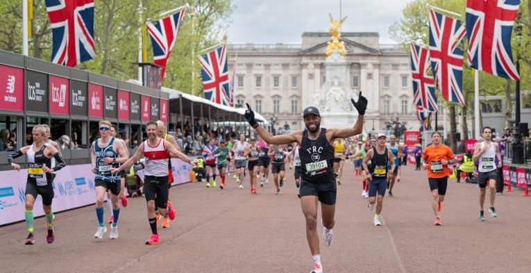 Person approaching the finish line with arms in the air. Multiple runners behind them. 