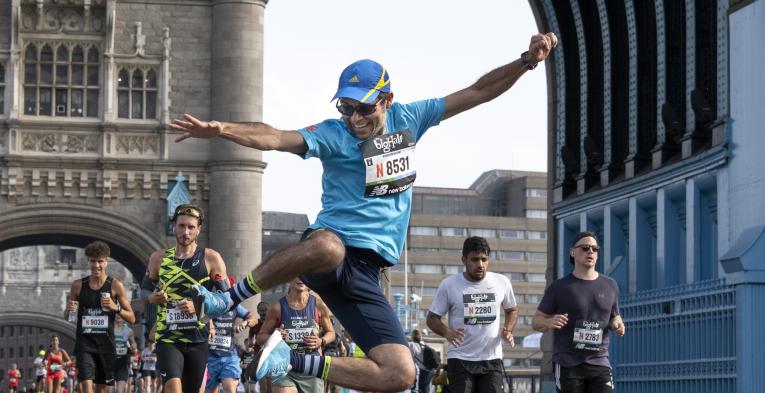 Man is jumping in the air clicking his heals on tower bridge as he competes in the big half.