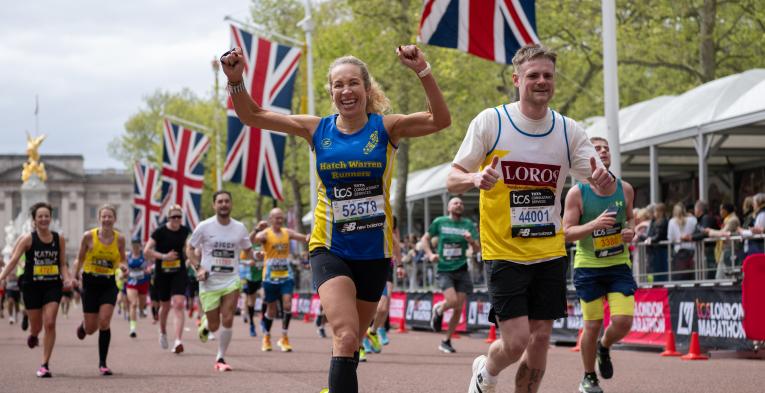 two people running, one with her arms in the air and one giving two thumbs up