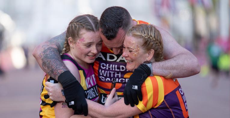 3 people embracing in a group hug wearing orange vests 