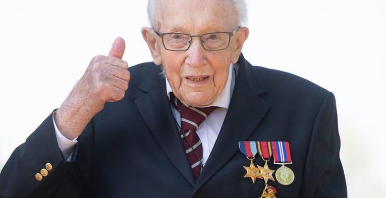 A well dressed man with medals and glasses gives a thumbs up.