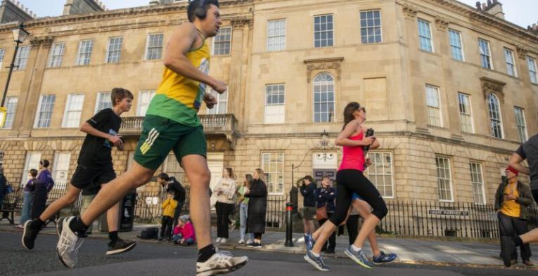 People running through Bath with sand stone buildings in the background.