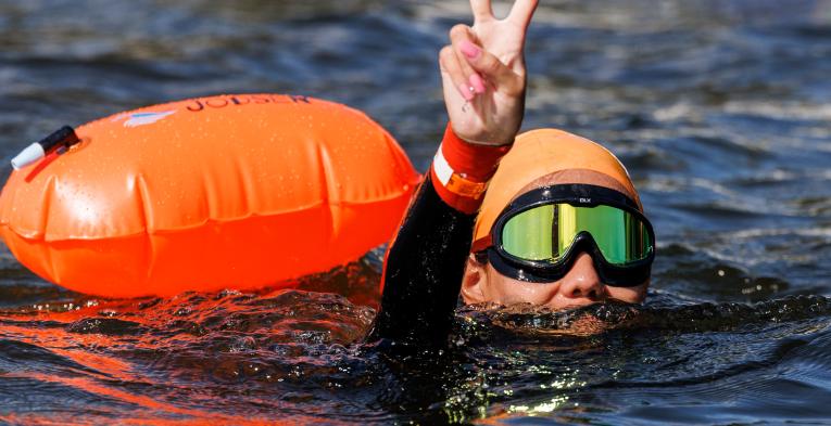 Swim Serpentine participant holds up a peace sign from the water