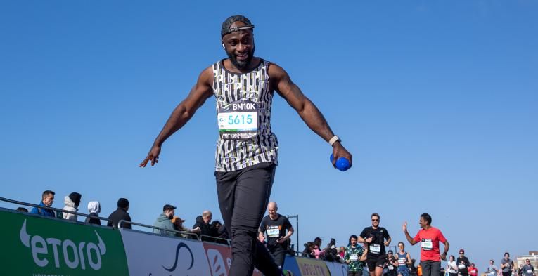 Man with arms outstretched smiling as he crosses the finish line at brighton 10k