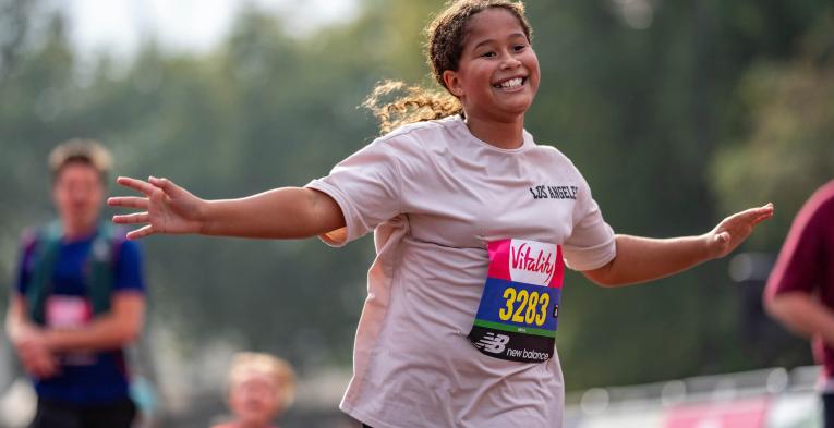 A young girl smiles with her hands out as she runs the Vitality Westminster Mile