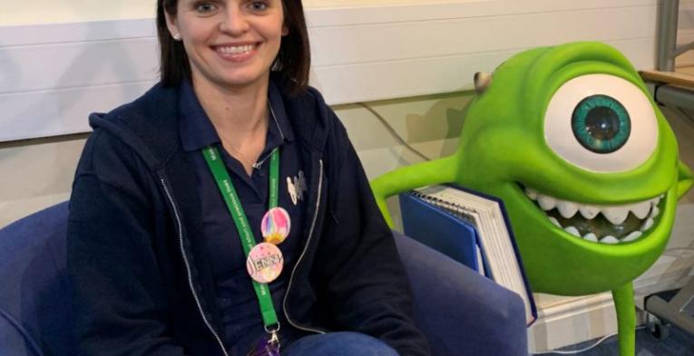  A lady smiling sitting next to a Disney character thing.