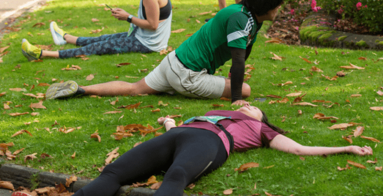 People lying down and stretching on the grass after running.