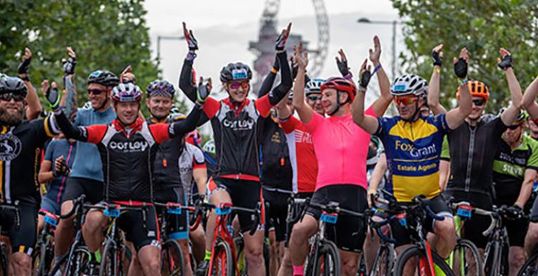 A bunch of cyclists in London with their hands raised.