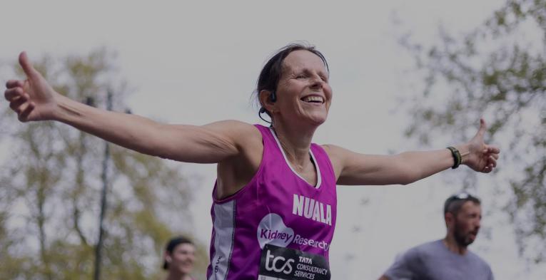 A runner with her arms out stretched in a charity running vest as she crosses the Finish Line