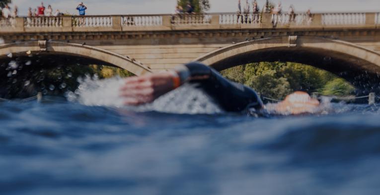 A swimmer shot from water level in front of the Serpentine bridge