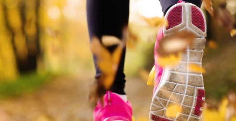 Pink shoes running through yellow autumn leaves.