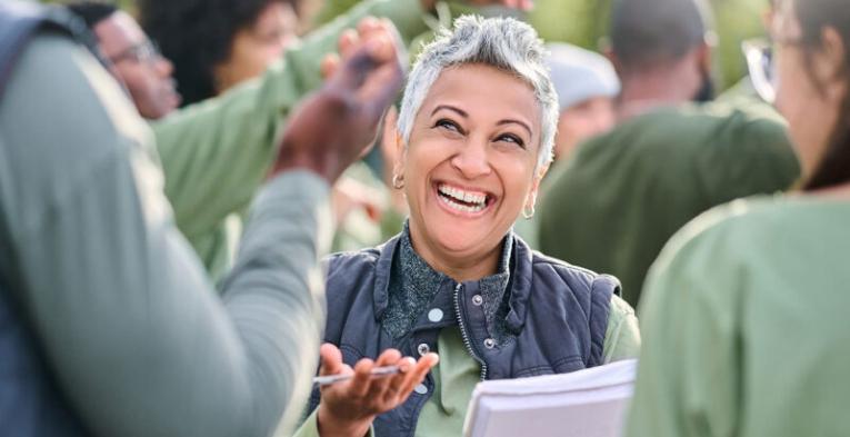 An excited woman at a running event smiling and holding a pen and books.