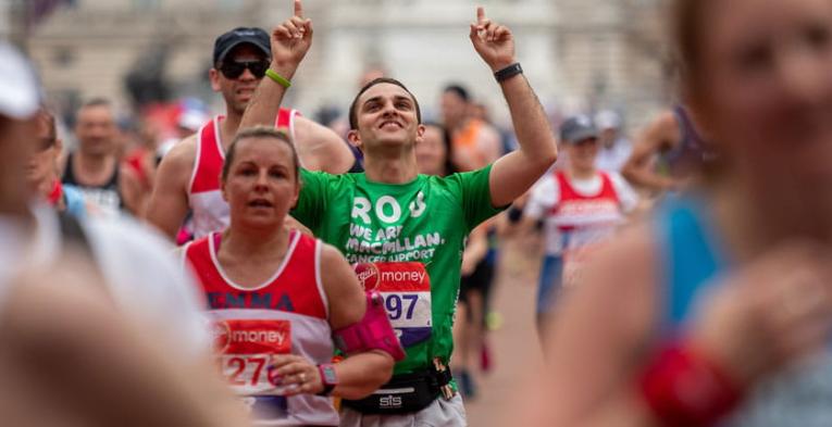 A macmillan charity runner points to the sky as he nears the finish line