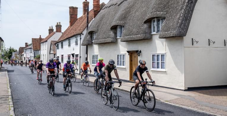 Cyclists ride past a thatched cottage