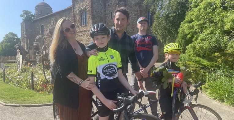 A family of cyclists stand in front of a small castle