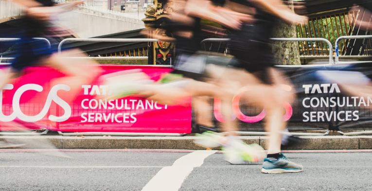 Runners run past some TCS branding