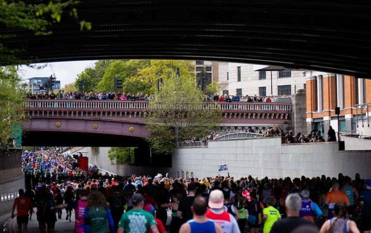 A photograph of runners running under a bridge lined with spectators