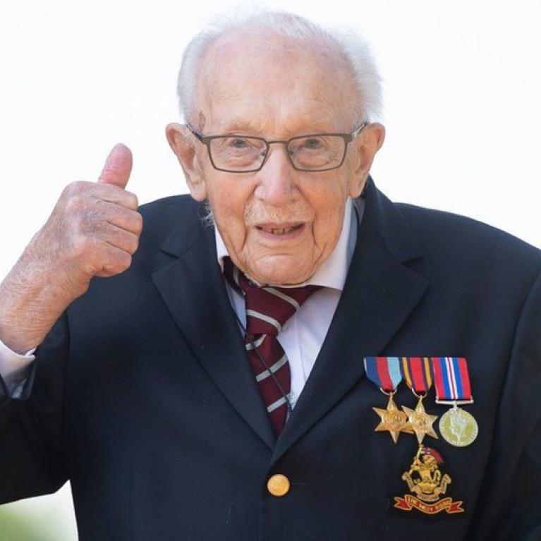 A well dressed man with medals and glasses gives a thumbs up.