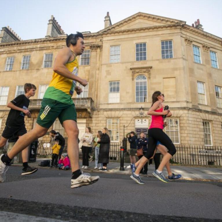 People running through Bath with sand stone buildings in the background.