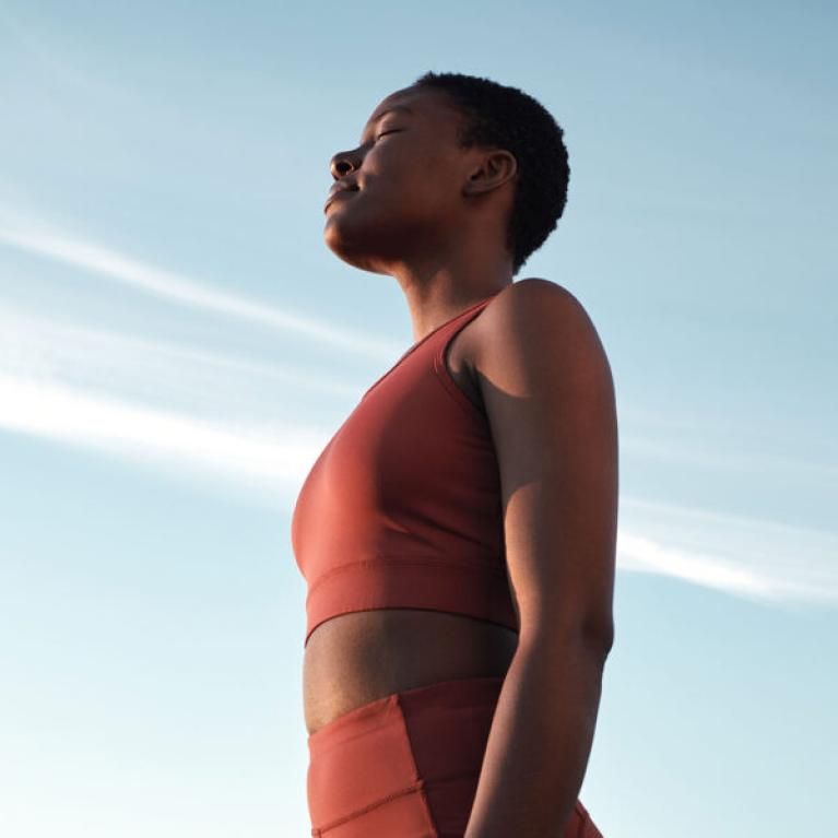 A woman embracing the sunshine in active sportswear with her eyes closed and head raised high.