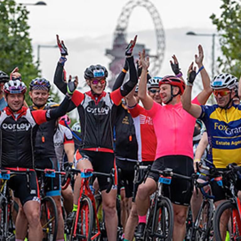 A bunch of cyclists in London with their hands raised.