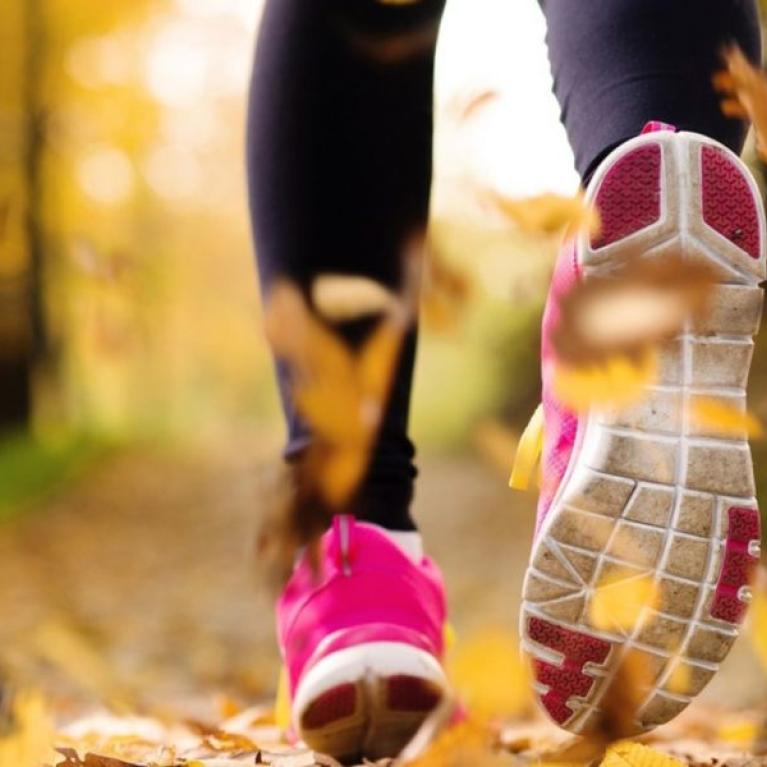 Pink shoes running through yellow autumn leaves.