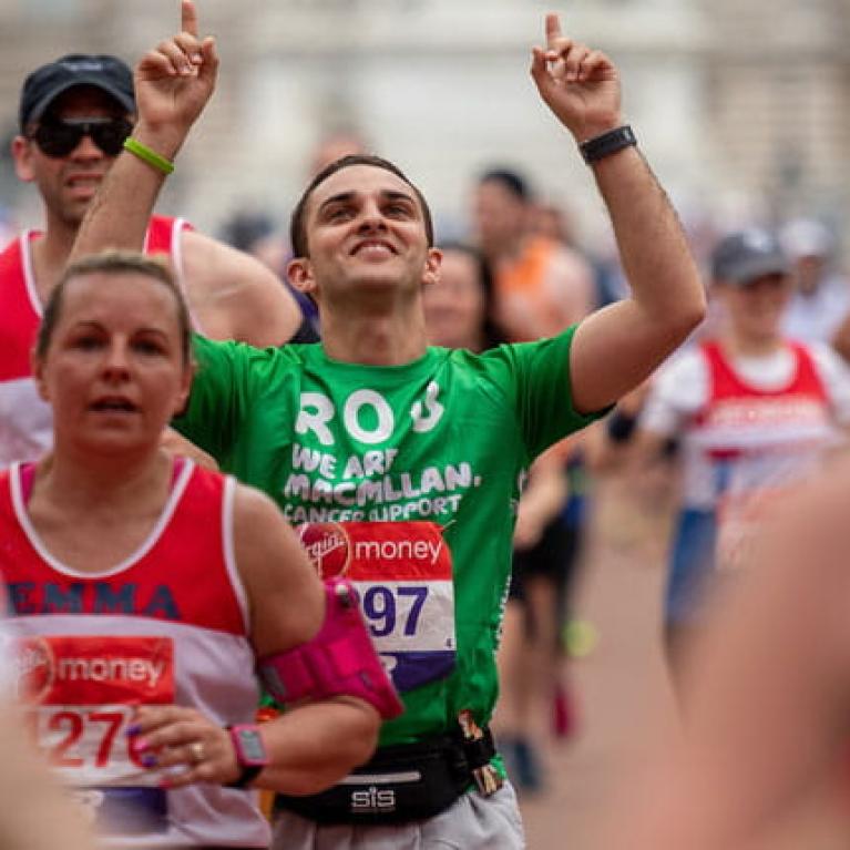 A macmillan charity runner points to the sky as he nears the finish line