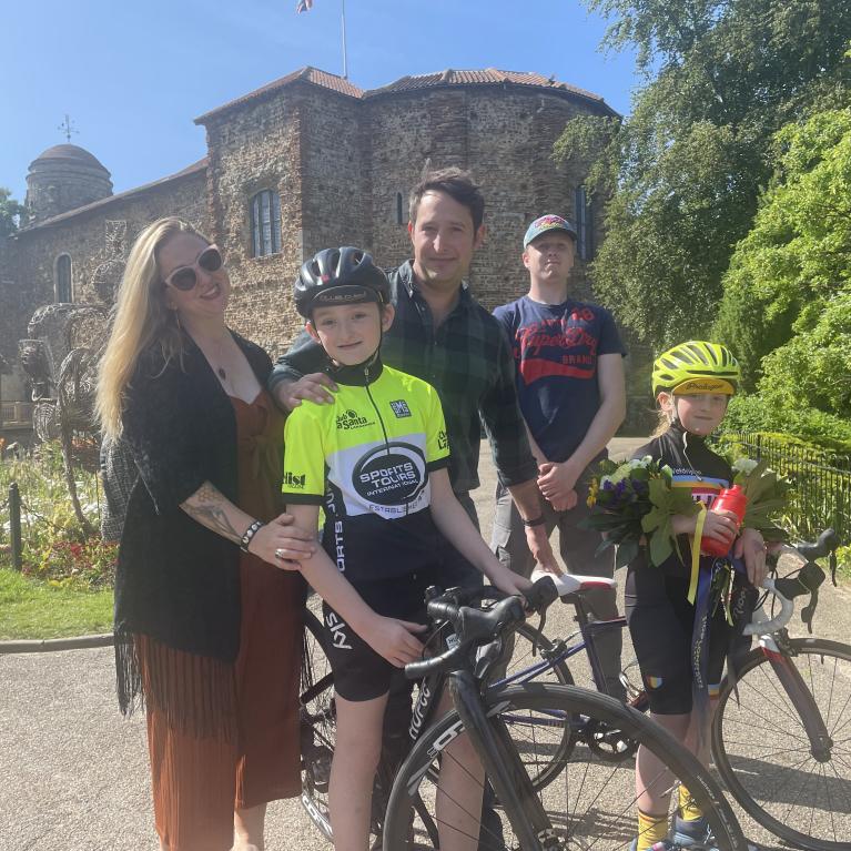 A family of cyclists stand in front of a small castle