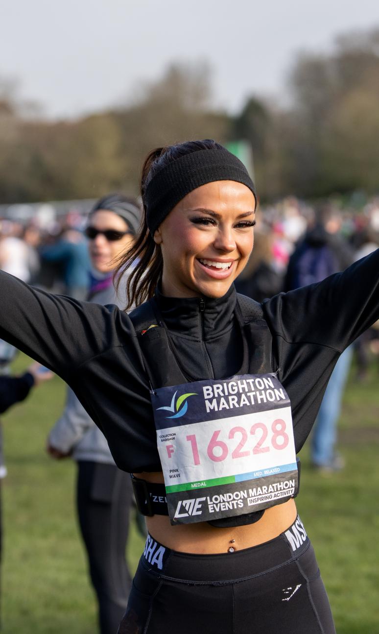 Woman in a headband and wearing a marathon number stands with arms out stretched