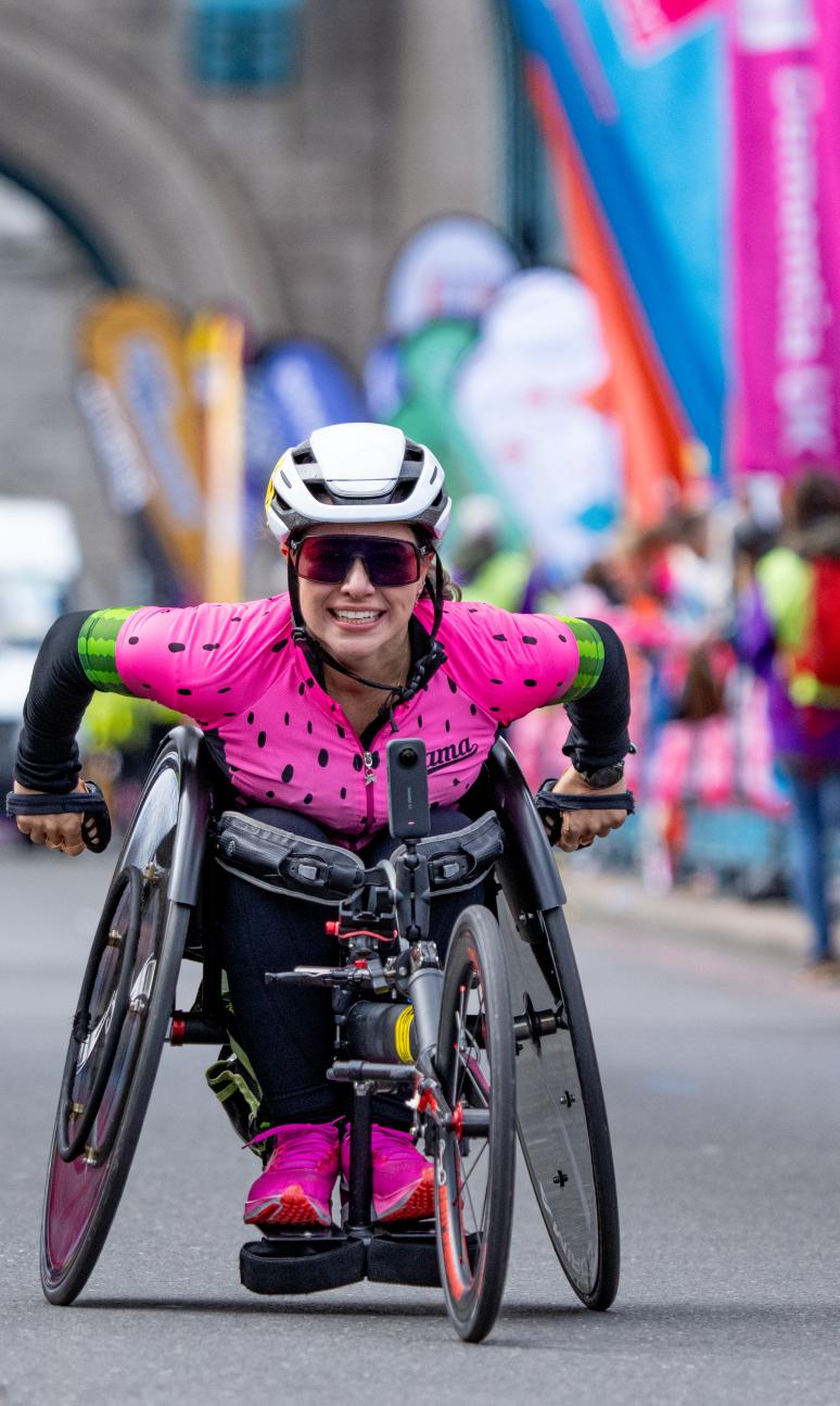 Woman in wheelchair and pink top smiles as she competes in London marathon