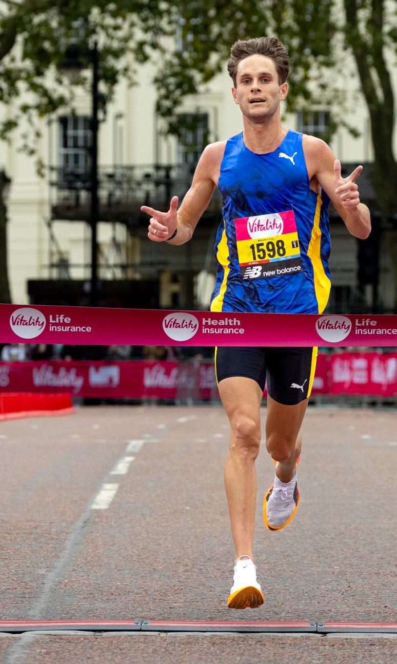 Man in blue vest running towards the finish line