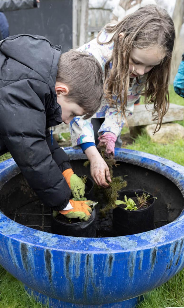 Two children planting in a large plant pot