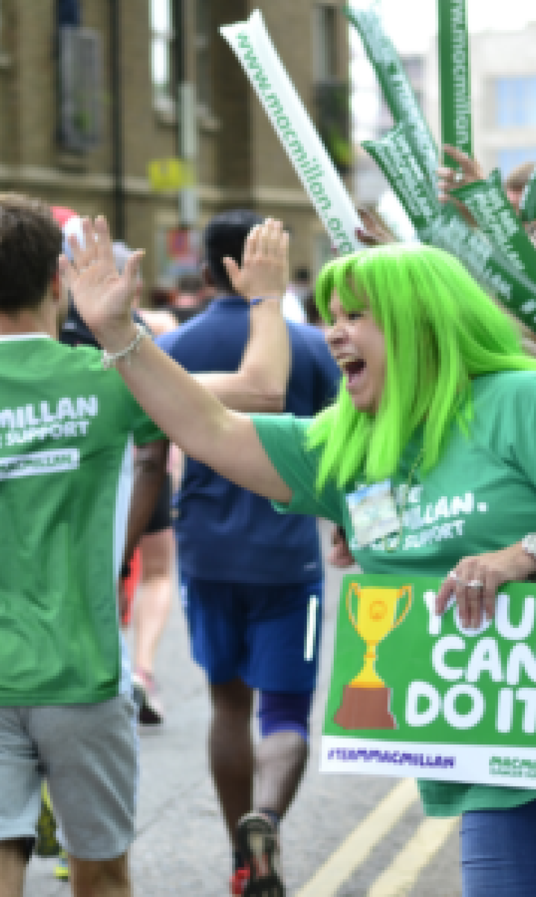 A Macmillan supporter high fives runners on the side of the route