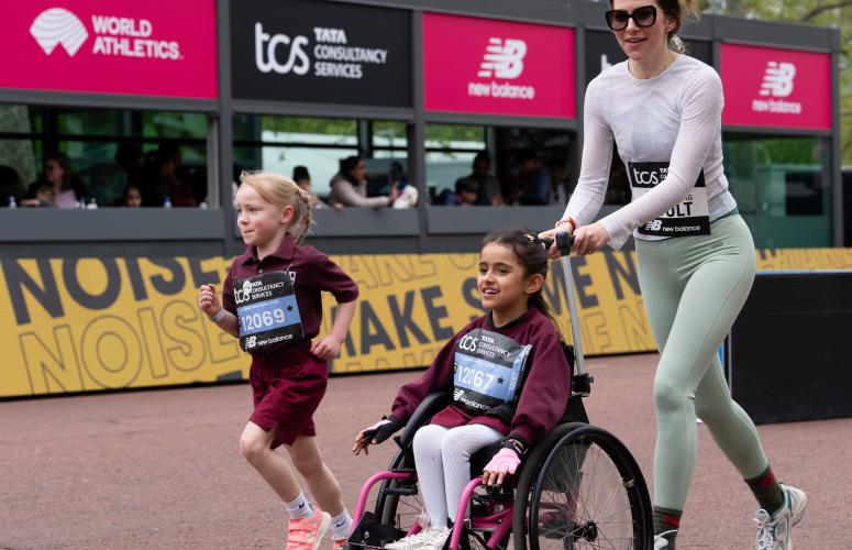 A person pushing a child in a wheelchair on the race course with another child running next to them