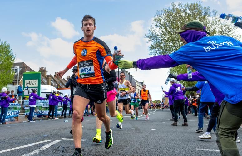 Person running in an orange top being handed a water by a volunteer