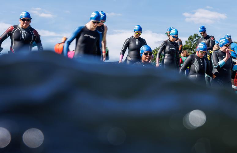 Water covers the bottom half of the image, above the waterline you can see a group of swimmers in wetsuits and googles waiting to start the Swim Serpentine event