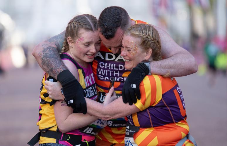 3 people embracing in a group hug wearing orange vests 