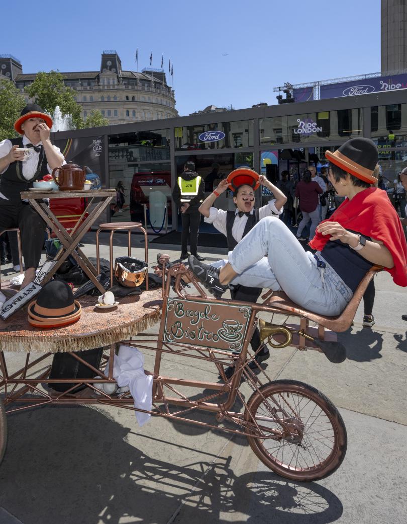 A woman interacts with two street performers at the RideLondon festival zone.