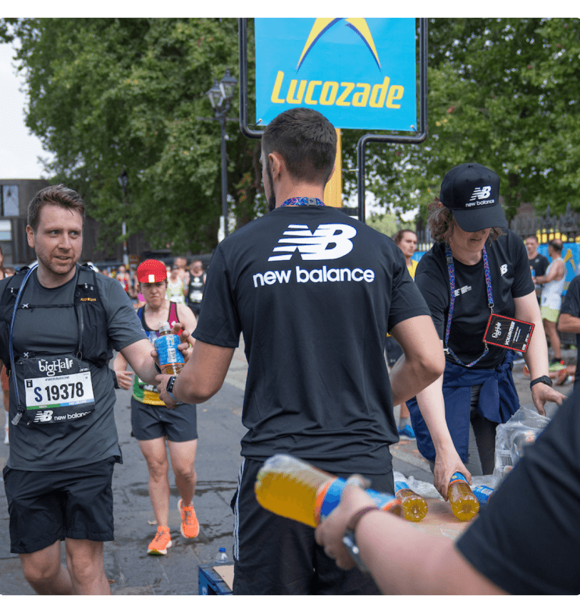 A volunteer with a New Balance tabard handing out drinks to participants